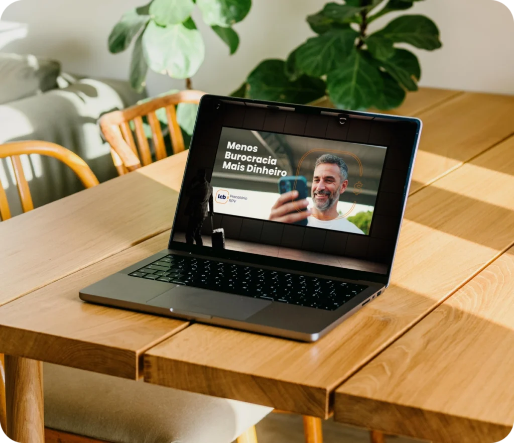 Laptop exibindo vídeo "Menos Burocracia Mais Dinheiro" com homem sorrindo.
